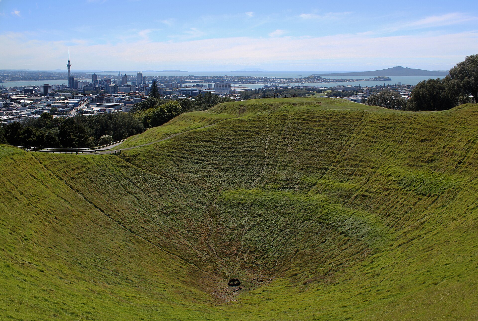 The grassy crater of Mount Eden with the Auckland CBD and Rangitoto Island behind it