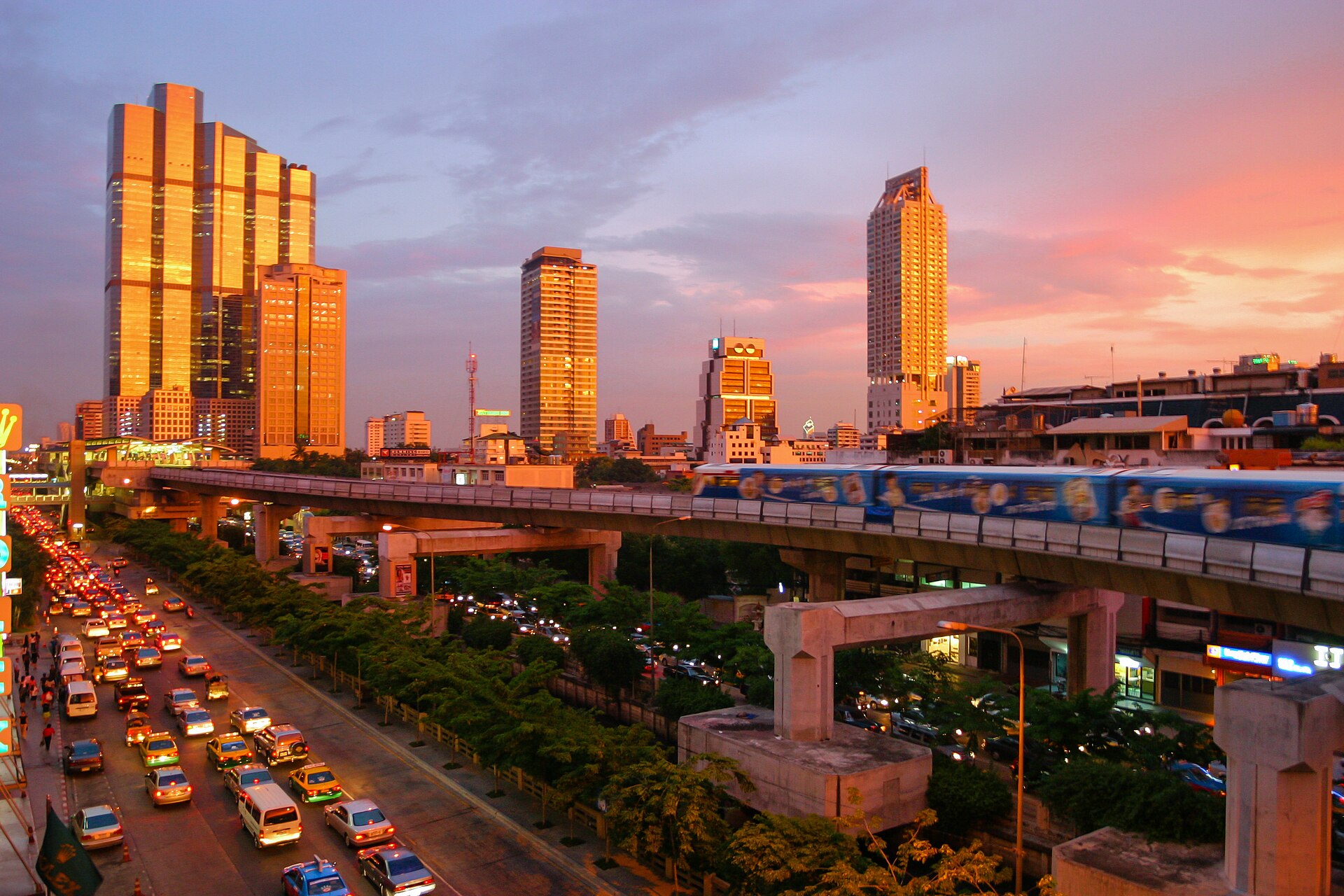 A BTS Skytrain train on elevated tracks above Bangkok traffic at sunset