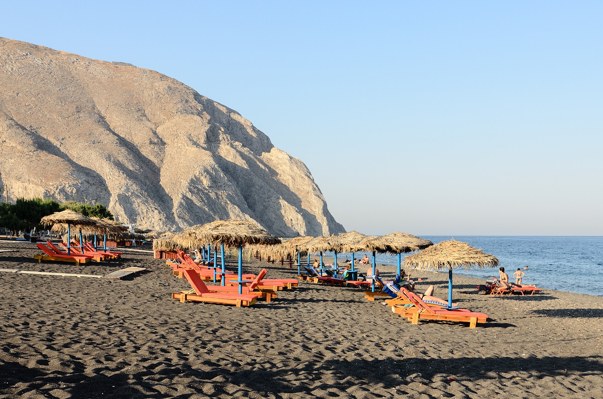 The black volcanic sand and sun loungers of Perissa beach on the south-east coast of Santorini