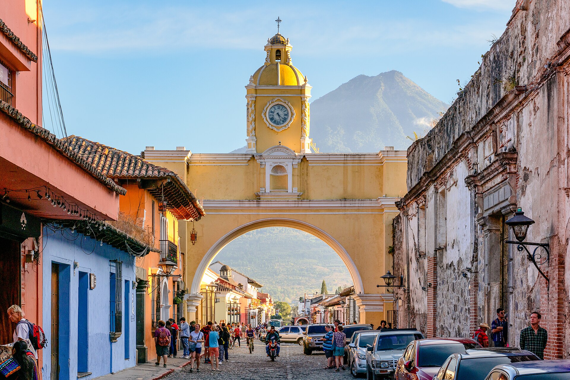 The yellow Santa Catalina Arch spanning a cobbled street in Antigua Guatemala with a volcano behind